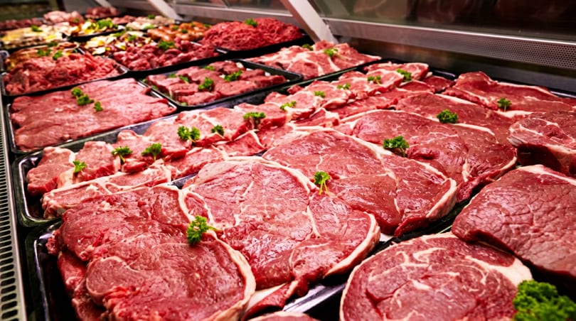 Various fresh red meat cuts, including steaks and ground beef, displayed in a refrigerated case with parsley.