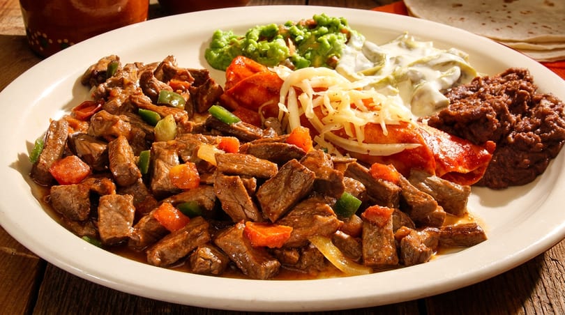 Mexican platter with beef stew, guacamole, rajas con crema, refried beans, and a cheese enchilada.